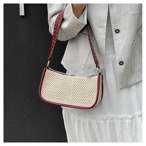 Detail of straw shoulder bag with red leather strap and silver studs on grey blazer