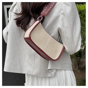Detail of straw woven underarm bag with burgundy leather strap and silver studs