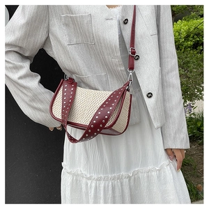 Detail of straw crossbody bag with silver studs on red leather wide shoulder strap