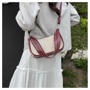 Outdoor shot of a woven shoulder bag with burgundy faux leather trim and silver rivets