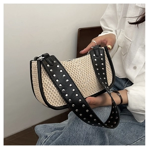 Close-up of woven straw crescent bag with black leather straps and silver metal rivets