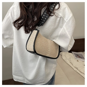 Close-up of beige woven straw bag with black silver studded strap on model shoulder