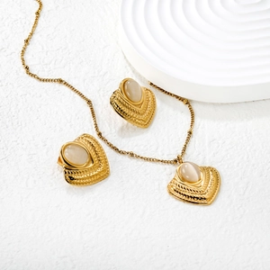 Vintage gold jewelry set with opal stone heart pendants on a textured stone surface