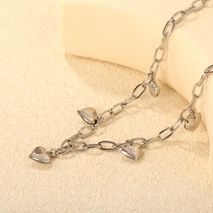 Polished stainless steel heart necklace with elegant charms on a minimalist textured base