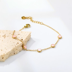 Detail of a gold stainless steel bracelet with five pink round shell charms on stone