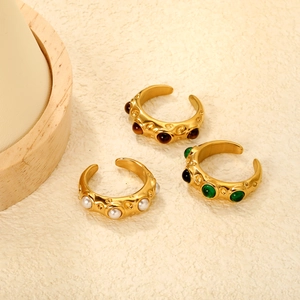 Close-up of three vintage gold rings with green, white, and amber stones on warm background
