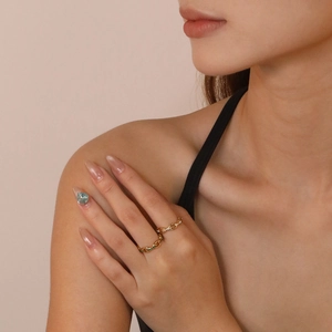 Close-up of a gold chain ring set with emerald and white stones on a model's finger