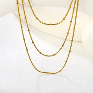 Minimalist 18K layered gold snake chain necklace with pearl accents on a white display