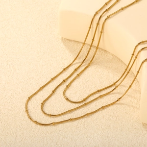 Three-layer gold beaded snake chain necklace displayed on a white textured stand