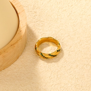Macro detail of 18K gold braided twisted ring with inlaid emerald green stones