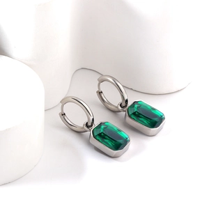 Polished silver earrings featuring rectangular emerald green crystals on white geometric props