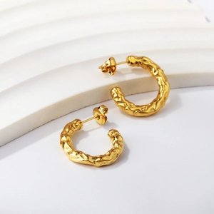 Détail de boucles d'oreilles créoles dorées en C avec texture martelée sur support blanc