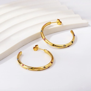 Détail de boucles d'oreilles dorées en C avec cristaux colorés sur un support blanc
