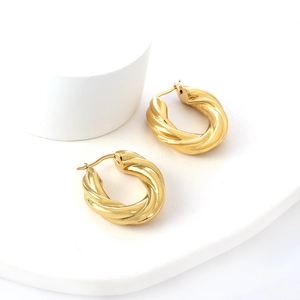 Gros plan de boucles d'oreilles créoles torsadées dorées sur support blanc minimaliste