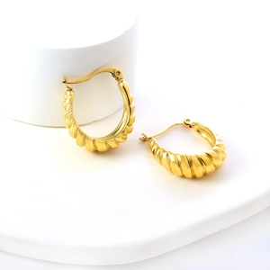 Détail des boucles d'oreilles dorées torsadées en forme de C sur socle blanc