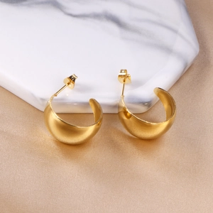 Détail de boucles d'oreilles dorées irrégulières en C sur fond de marbre