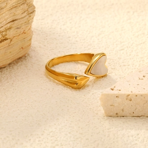 Dettaglio macro dell'anello dorato aperto con intarsio a cuore bianco e texture martellata