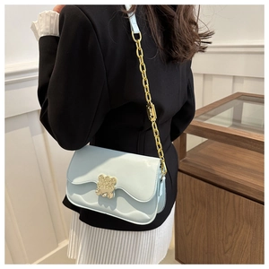 Détail d'un sac bleu clair avec fermoir doré en forme d'ours et bandoulière chaîne