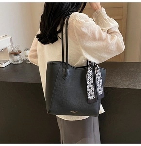 Detailed view of black pebbled leather tote bag with a decorative checkered scarf and logo