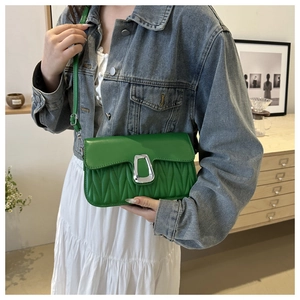 Model wearing a bright green pleated shoulder bag with silver buckle in a modern home