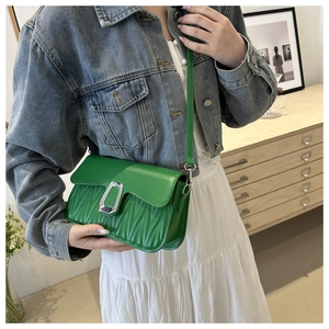 Green pleated crossbody bag with silver U-shaped buckle styled on a denim jacket