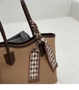 Detail of tan pebble leather tote bag featuring decorative argyle silk scarf on handle