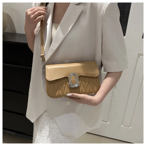 Detail of light brown quilted crossbody bag featuring a silver square buckle on white suit