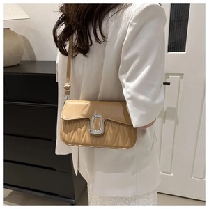 Detail of apricot quilted crossbody bag with large silver buckle on a female model