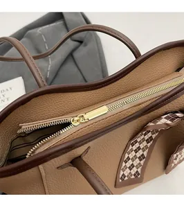 Detail of smooth gold metal zipper and lychee pattern leather texture on a brown tote