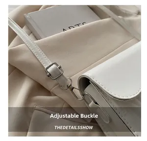 Close-up of adjustable metal buckle and strap on white leather shoulder bag
