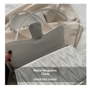 Detail of metal magnetic buckle and V-shaped quilted texture on a white crossbody bag