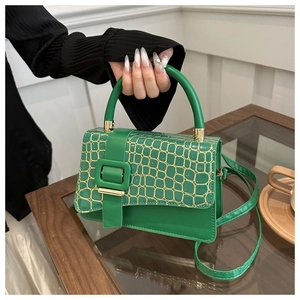 Detail of dark green crocodile texture handbag with gold hardware and flap closure