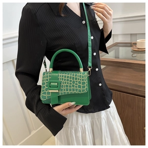 Detail of green faux crocodile texture handbag with golden buckle and adjustable strap
