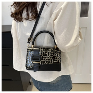 Detail of black handbag with crocodile texture flap and decorative gold square buckle
