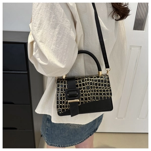 Detail of elegant black crossbody bag with gold-trimmed crocodile texture on the flap
