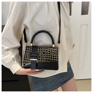 Detail of black crossbody bag with gold-trimmed crocodile pattern and leather handle