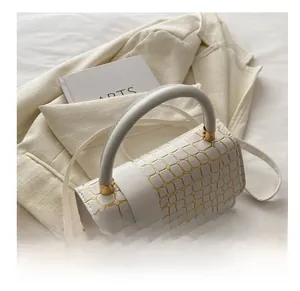 Detail of white crocodile embossed leather handbag on a beige suit with artsy book