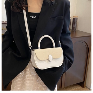 Detail view of a white leather crossbody bag with beige woven flap on a female model