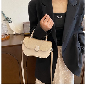 Detail of cream crossbody bag featuring woven texture flap and metallic oval clasp