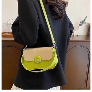 Dettaglio borsa in pelle verde con patta in paglia indossata su un blazer nero