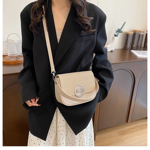Detail of a beige contrast box bag featuring a round silver buckle and textured flap