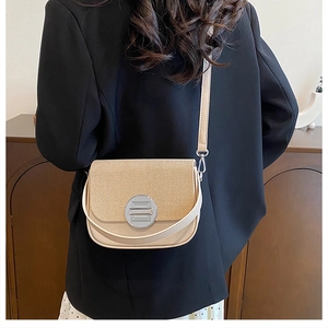 Detail of stylish beige crossbody bag with textured flap and metal clasp on black blazer