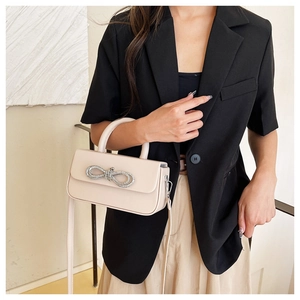 Detail of light beige structured bag featuring a silver rhinestone bow and leather strap
