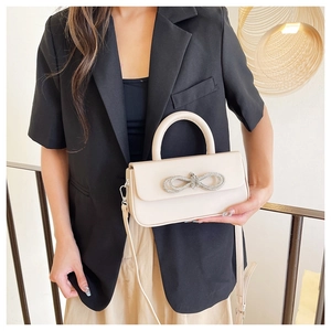 Detail of cream structured handbag featuring a sparkling rhinestone bow and crossbody strap