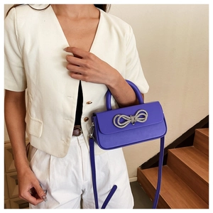 Detail of purple crossbody box bag with sparkling rhinestone bow and smooth leather texture