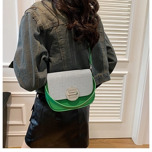 Detail of green leather box bag with striped flap and metal lock on a model's shoulder