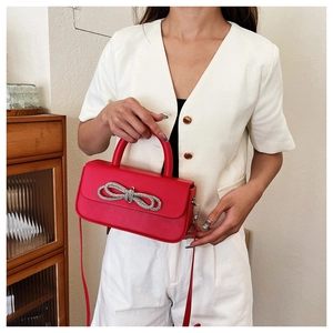 Detail of a red crossbody box bag featuring a sparkling crystal bow and top handle
