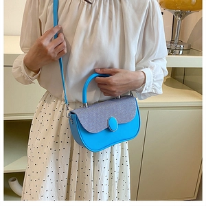 Detail of blue crossbody box bag with striped flap held by model in indoor setting