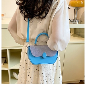 Detail of blue leather and textured fabric patchwork handbag worn with a white dress