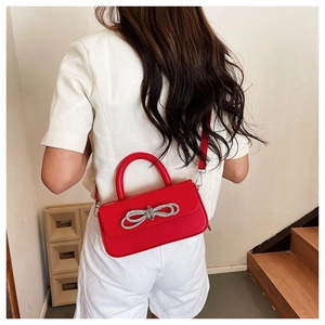Macro view of red crossbody bag with silver rhinestone bow and leather top handle